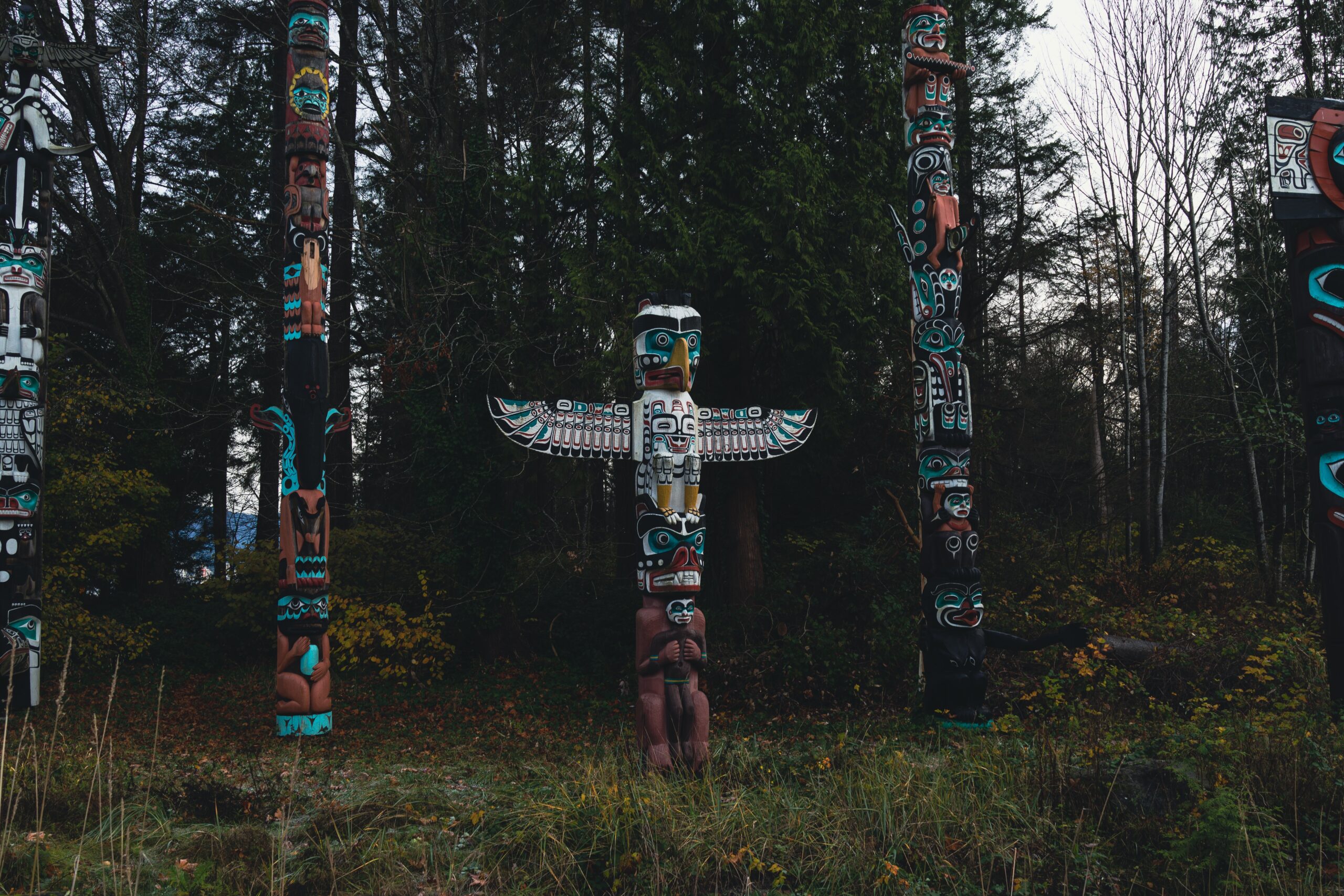 A field with Indigenous totem poles against a background of forest